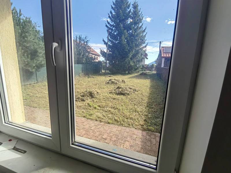 A view from a family house in Ľubela into a garden with a well-maintained lawn and trees.