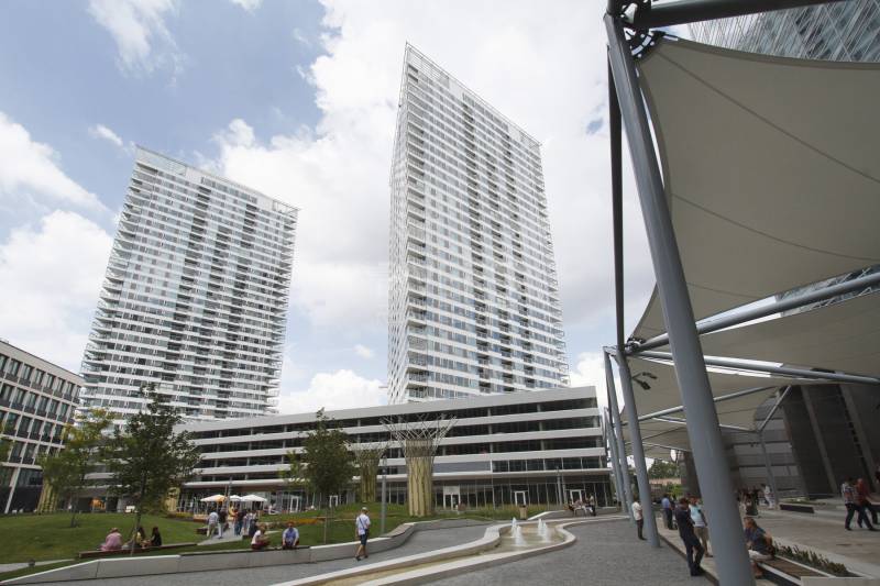 High-rise buildings in the area on Landererova Street, people relaxing by the fountain and trees.