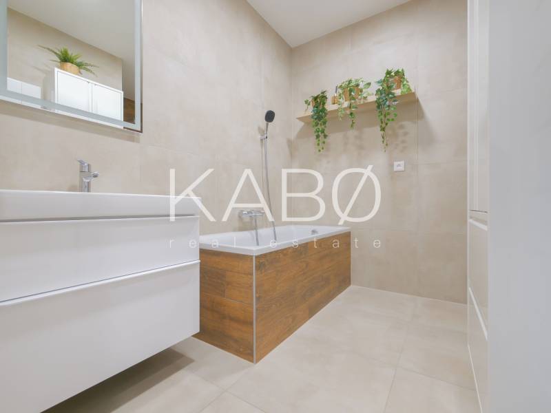 A bathroom in a family house with a bathtub, plants, and cabinets, with a wooden decor floor.