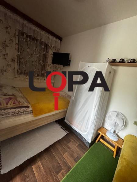 The interior of the cabin includes a bed, a cabinet, a fan, and a floor with a wooden decor.