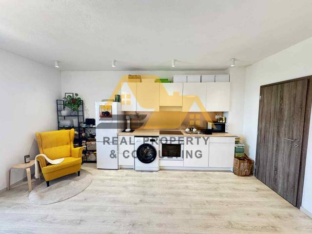 A kitchen in a 2-room apartment with white cabinets and a yellow chair, a floor with a wooden decor.