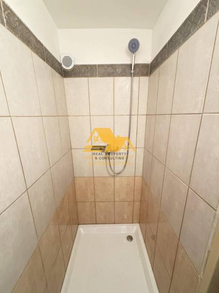 Tiled shower corner in a 2-room apartment with a simple design and a showerhead.