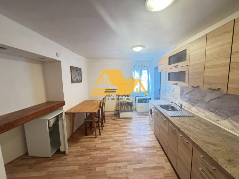 A kitchen in a 2-room apartment with wooden floor decor and light furniture.
