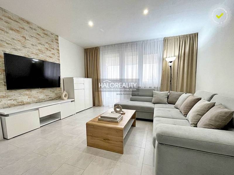 Living room in a two-room apartment with a sofa, television, and wooden decor flooring.
