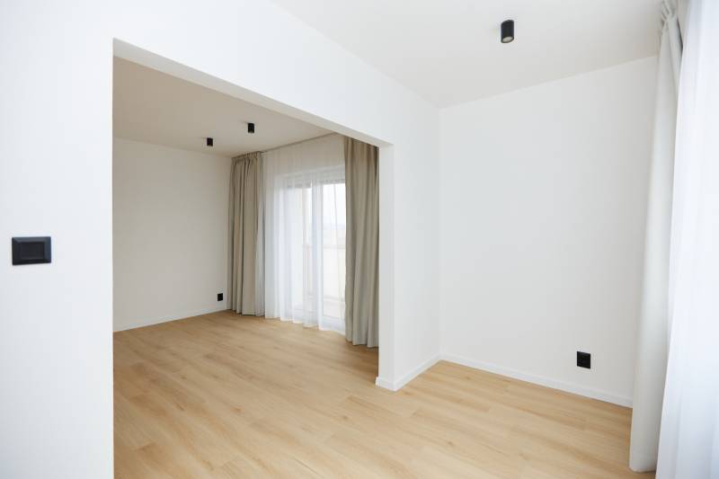A room in a 3-room apartment with a wooden decor floor, curtains, and a French window.