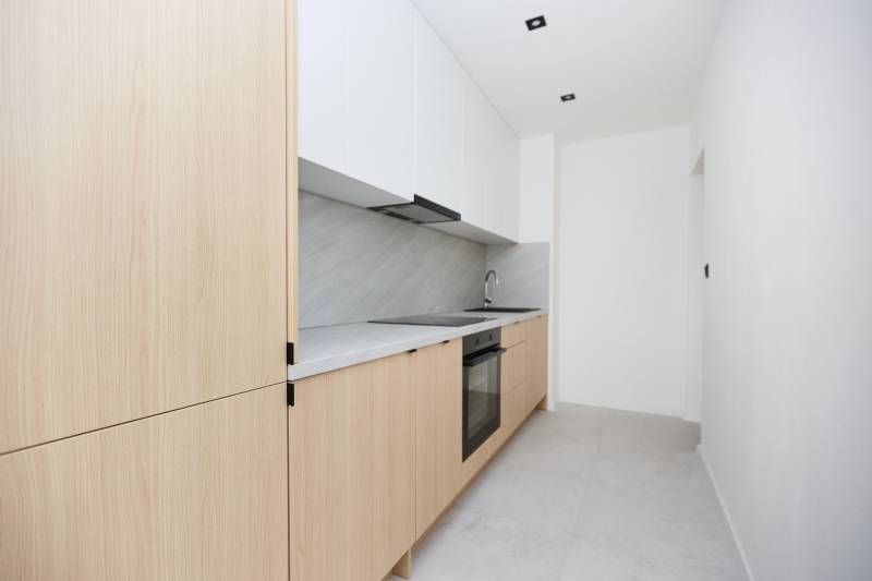 A minimalist kitchen in a 3-room apartment with wooden decor and white cabinets.
