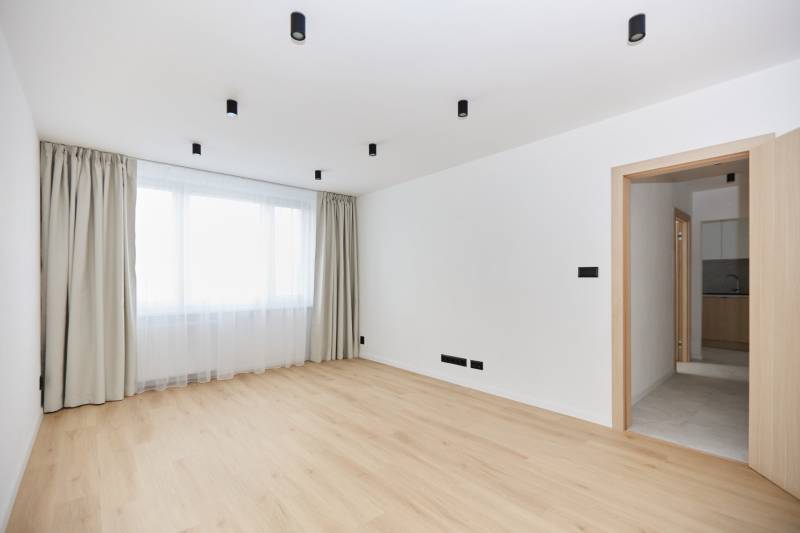 A spacious room with a wooden decor floor and a large window in a 3-room apartment.