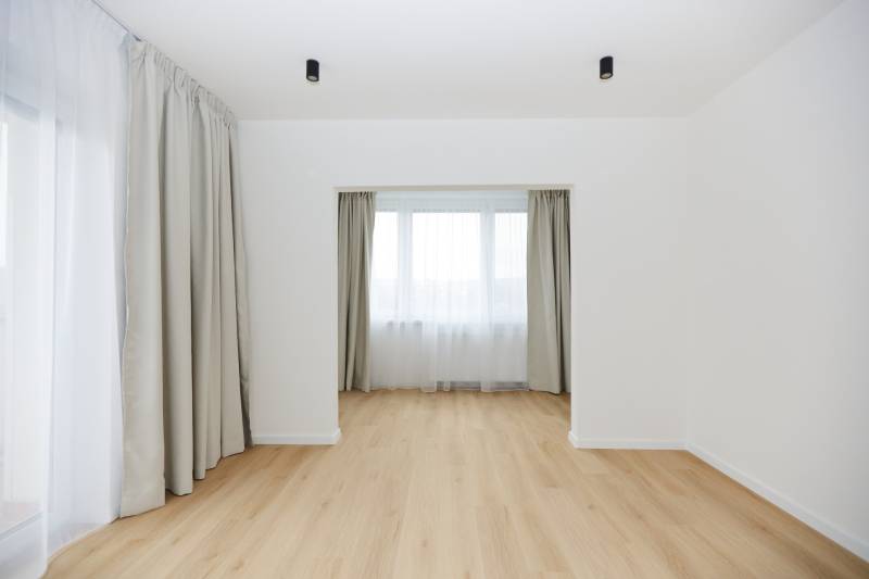 A room in a 3-room apartment with a wooden decor floor and large windows with curtains.