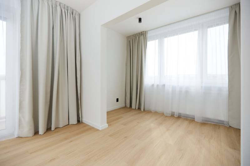A room with a wooden decor floor and large windows in a 3-room apartment.
