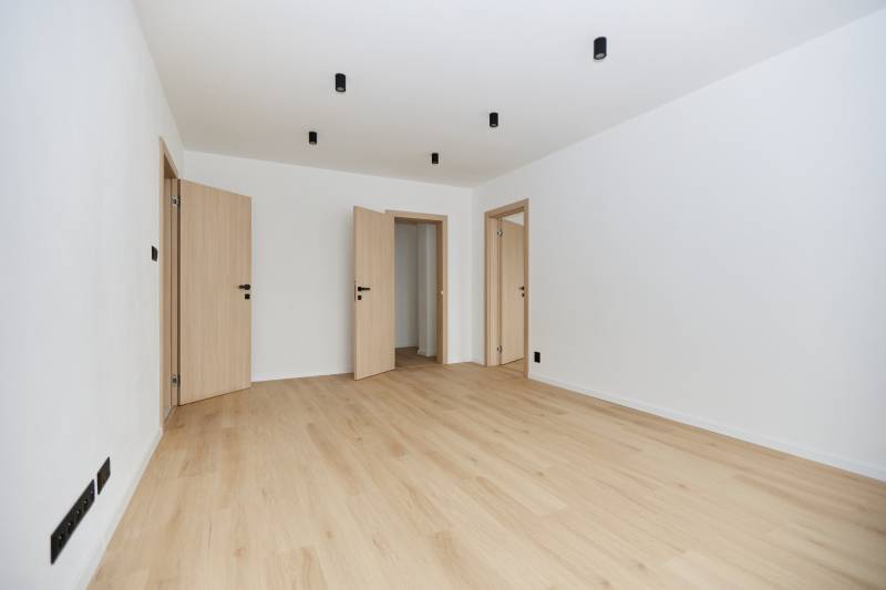 A spacious room in a 3-room apartment with a wood-decor floor and light-colored doors.