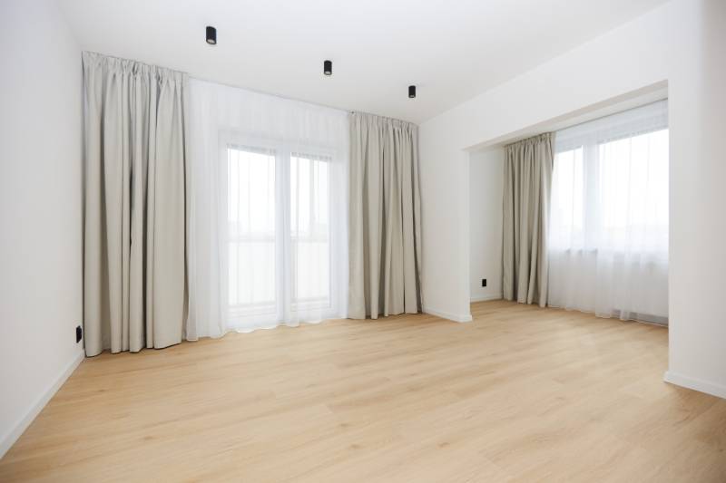 A room in a 3-room apartment with a wooden decor floor and large windows.