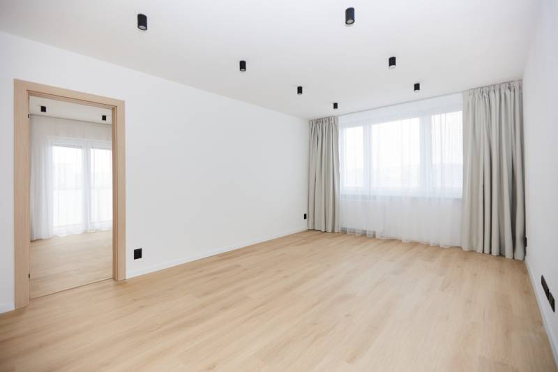 A spacious room in a 3-room apartment with a wooden decor floor and curtains.