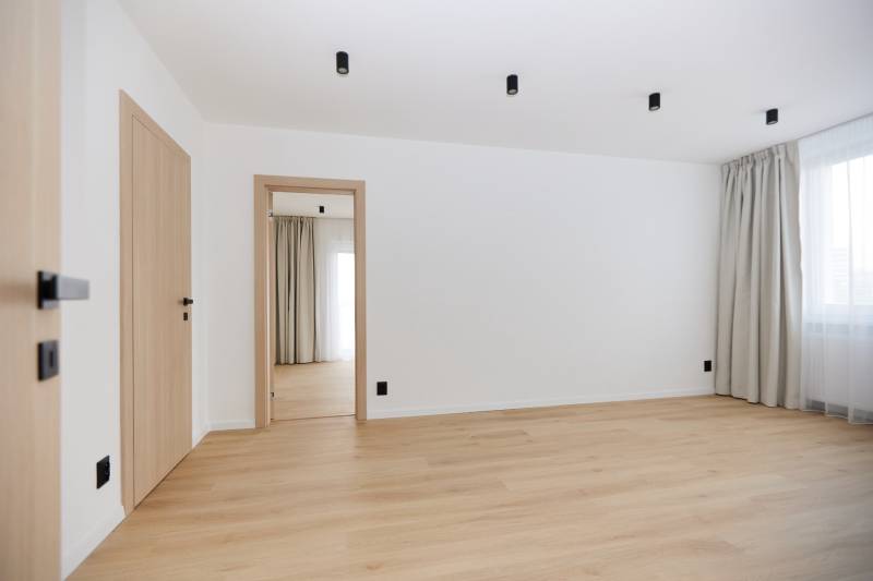A room with white walls, a floor with a wooden decor, and curtains in a 3-room apartment.