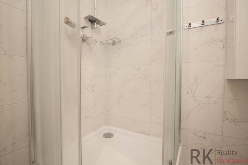 A shower enclosure in the bathroom with white marble tiles in a 3-room apartment.