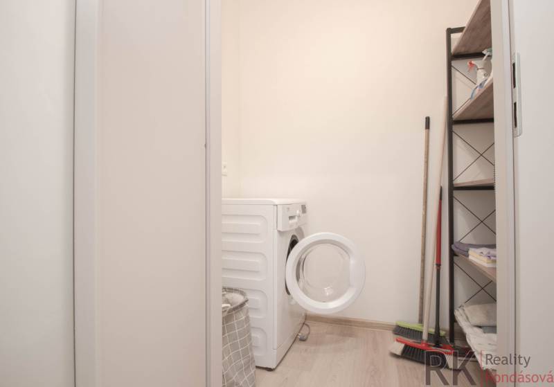 Laundry room in a 3-room apartment with a washing machine, shelf, and cleaning supplies.