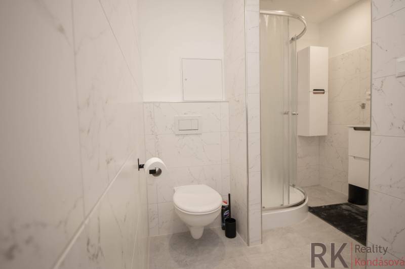 A bathroom with a shower, toilet, and white tiles in a 3-room apartment.