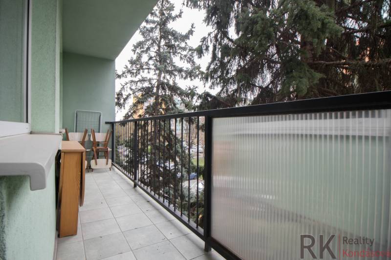 Balcony of a 3-room apartment with furniture and railing, view of greenery.