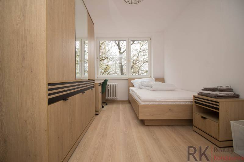 Bright bedroom in a three-room apartment with wood-patterned flooring and large windows.