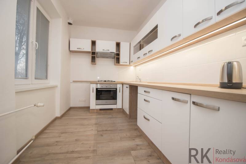A kitchen with appliances, white cabinets, and a wood-patterned floor in a two-room apartment.