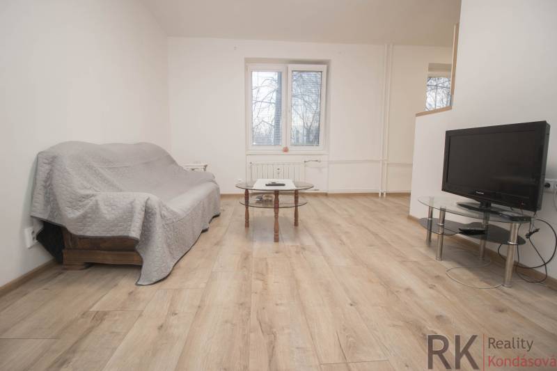 Living room in a two-room apartment with a sofa, table, and television on a floor with a wooden decor.