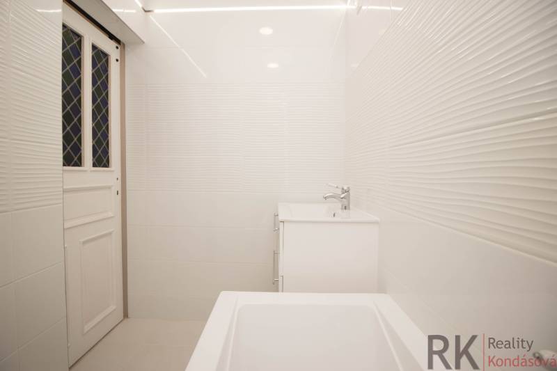 Bathroom in a 2-room apartment with white tiles, a sink, and a bathtub.