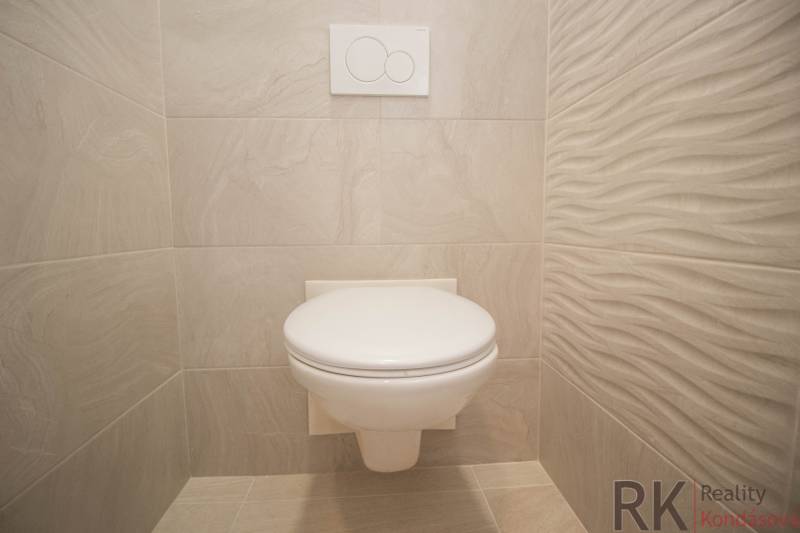 A bathroom in a two-room apartment with a white toilet and light tiles.