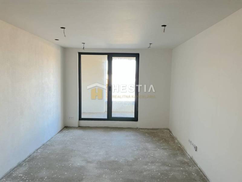 An empty room with a concrete floor, a balcony view, and a large window, suitable for a 2-room apartment.