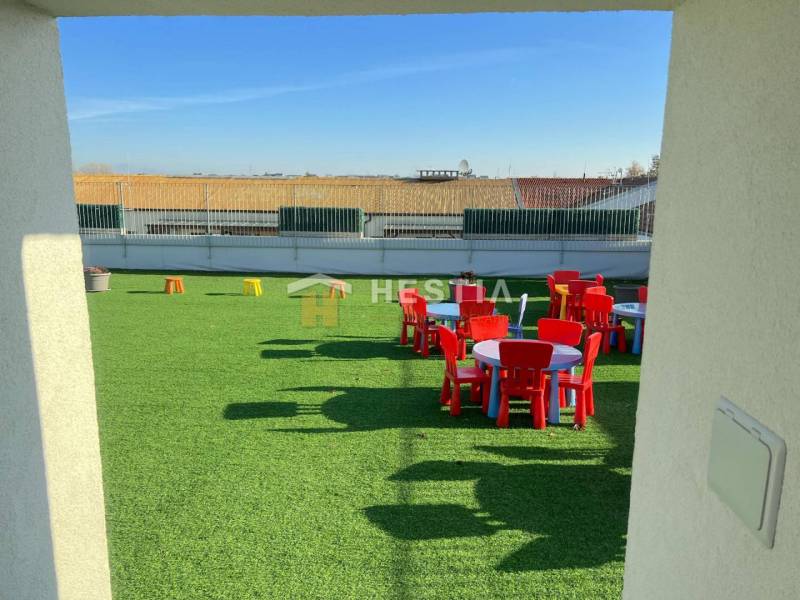 A playground on the roof with green artificial grass and colorful tables and chairs.
