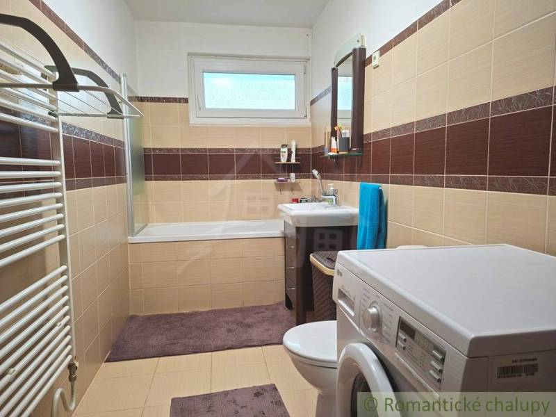 Bathroom in a family house with a bathtub, washing machine, and brown-beige tiles.