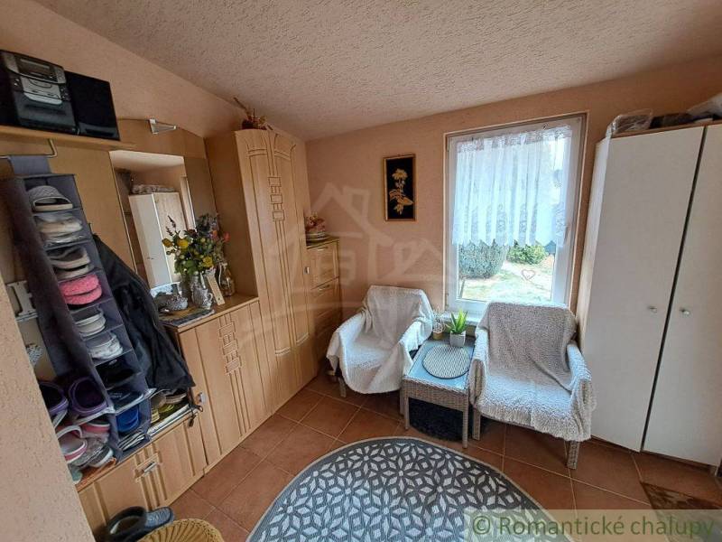 A view into the hallway of a family house with chairs, cabinets, and a window with a view.