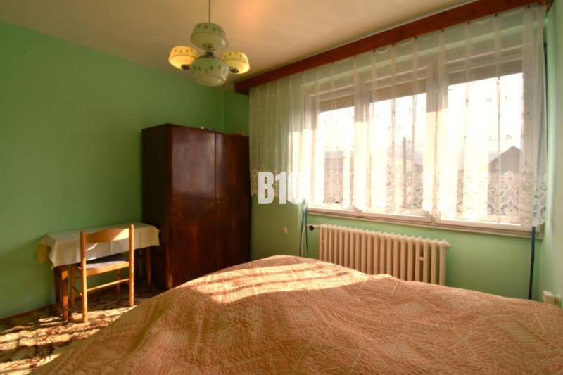 A bedroom in a family house with a window, curtains, a wardrobe, and a table.