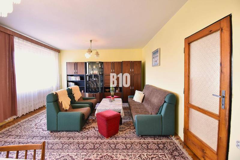 Living room in a family house with sofas, armchairs, a display cabinet, and a carpet.