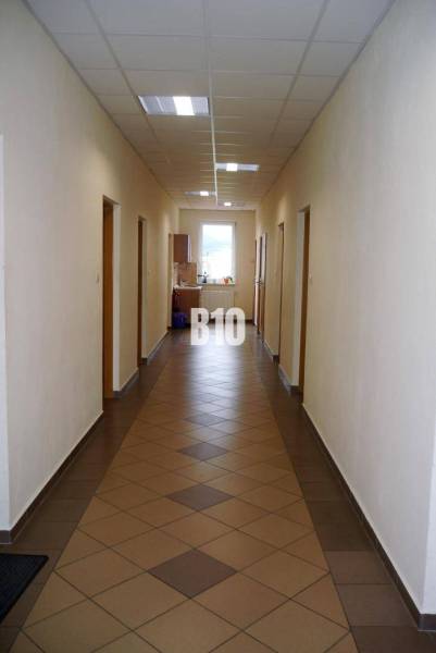 Hallway in an office with tiles, doors, and a window, interior lit by artificial light.