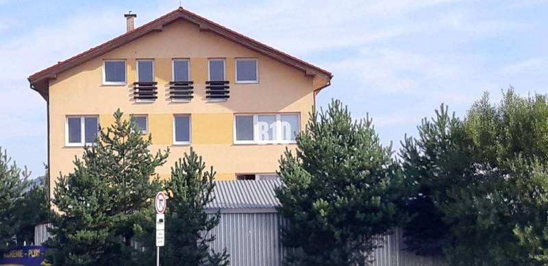 Yellow house with a sloped roof and windows behind trees near the office lines.