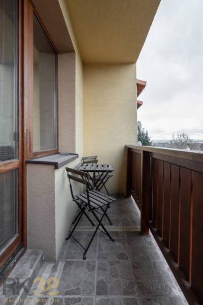 A balcony with a wooden railing and a table with two chairs in a 5 or more room apartment.
