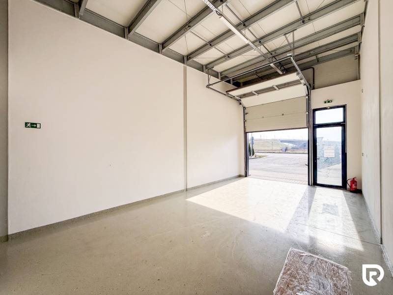 Commercial premises with a large garage door and gray flooring with lighting.