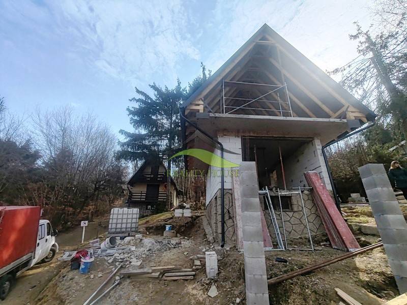 A cottage construction on Zajačia debra in Holčíkovce surrounded by trees and building materials.
