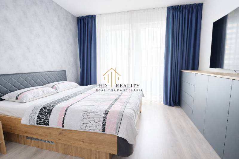 A bedroom in a 3-room apartment with a bed, blue curtains, and a dresser.