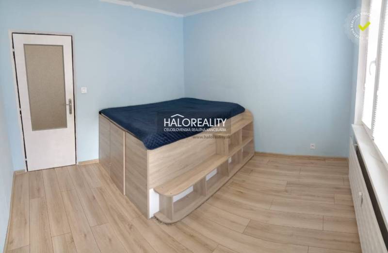 A bedroom with a raised bed and a wooden decor floor in a 3-room apartment.