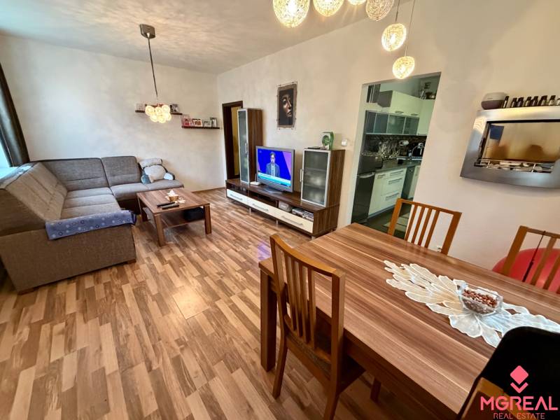 Living room in a three-room apartment with a wooden decor floor, a sofa, and a television.
