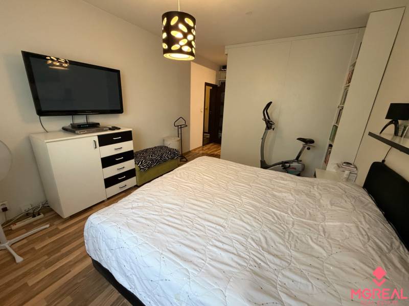 Bedroom in a 3-room apartment with a bed, television, and wooden decor flooring.
