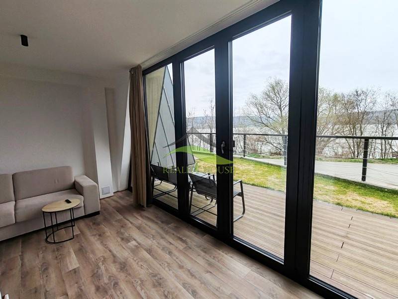 Interior of a cabin with a sofa, wooden decor flooring, large windows with a view of the terrace.
