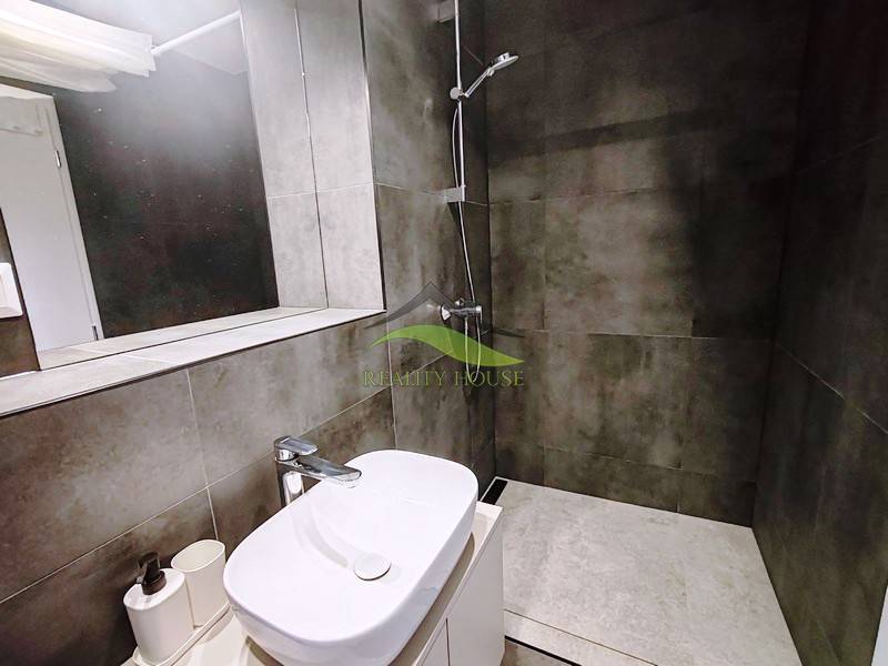 A bathroom in a cabin with a sink, mirror, and shower stall with dark tiles.