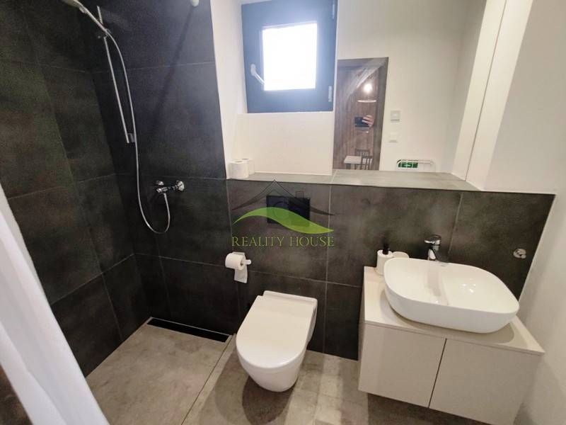 A bathroom in a cabin with a shower, modern sink, and toilet on a floor with a wooden decor.