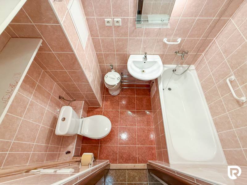 A bathroom in a studio apartment with a bathtub, sink, and toilet. Pink wall tiles.