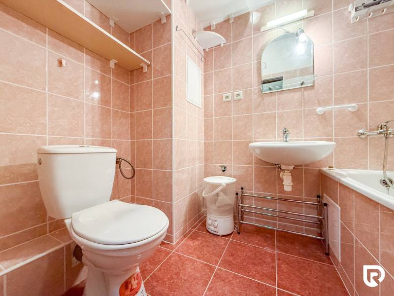 A bathroom in a studio apartment with a toilet, sink, bathtub, and tiles in a pink shade.