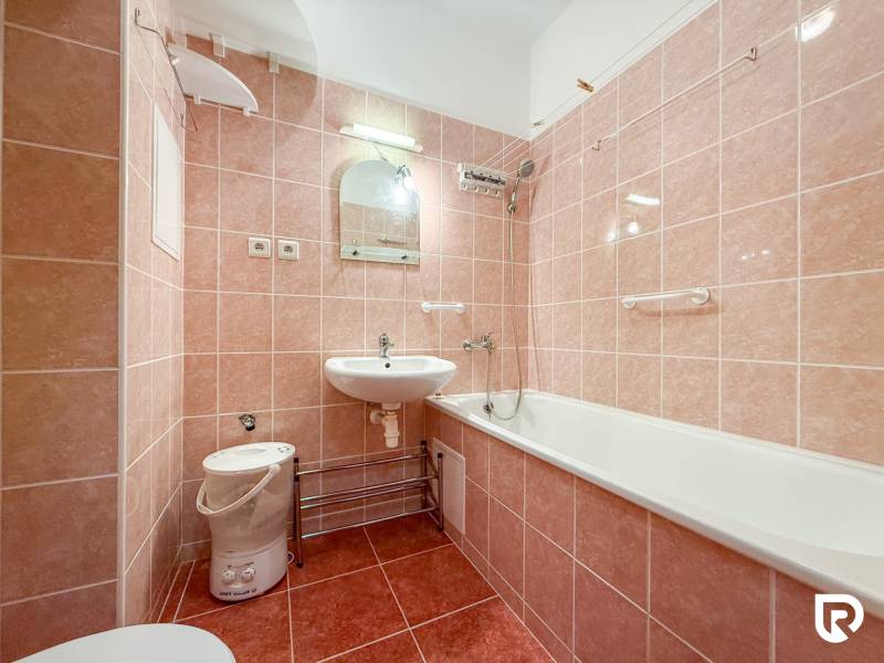 A bathroom in a studio apartment with pink tiles, a sink, and a bathtub.