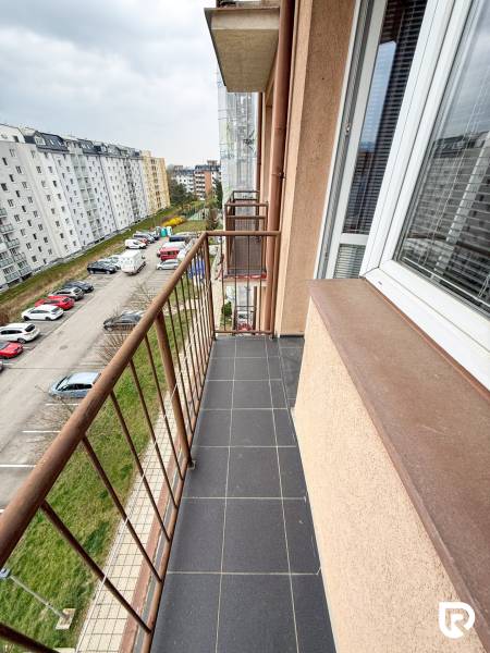 The balcony of a studio apartment on Východná Street in Trenčín with a view of the parking lot and buildings.