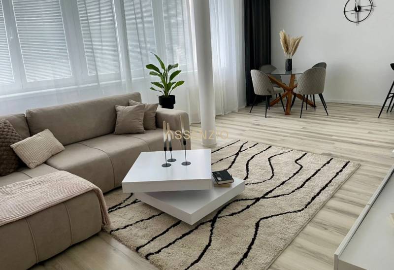 Bright living room with a sofa, coffee table, dining table, and wood-patterned flooring.