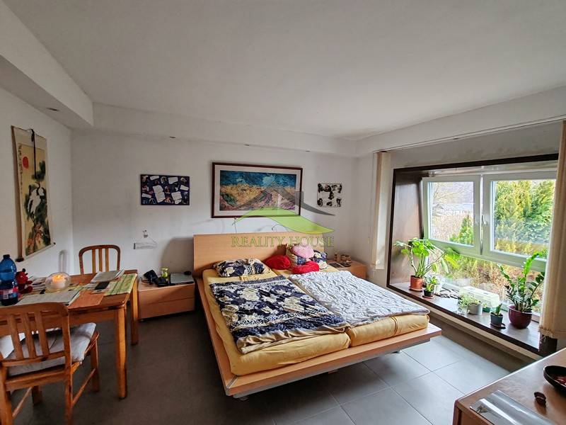 A bedroom in a family house with a desk and a large window, plants on the windowsill.